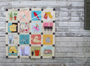 Finished quilt top featuring gardening motifs: watering can, boots, birdhouse, gloves, and more.