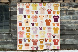 Graphic Tee Quilt hanging on a barn with weathered wooded boards. The quilt is made of a variety of fussy cut, foundation paper pieced, t-shirt quilt blocks.
