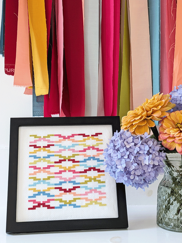 Modern cross stitch pattern called Interlock in a simple black frame next to a vase of flowers.