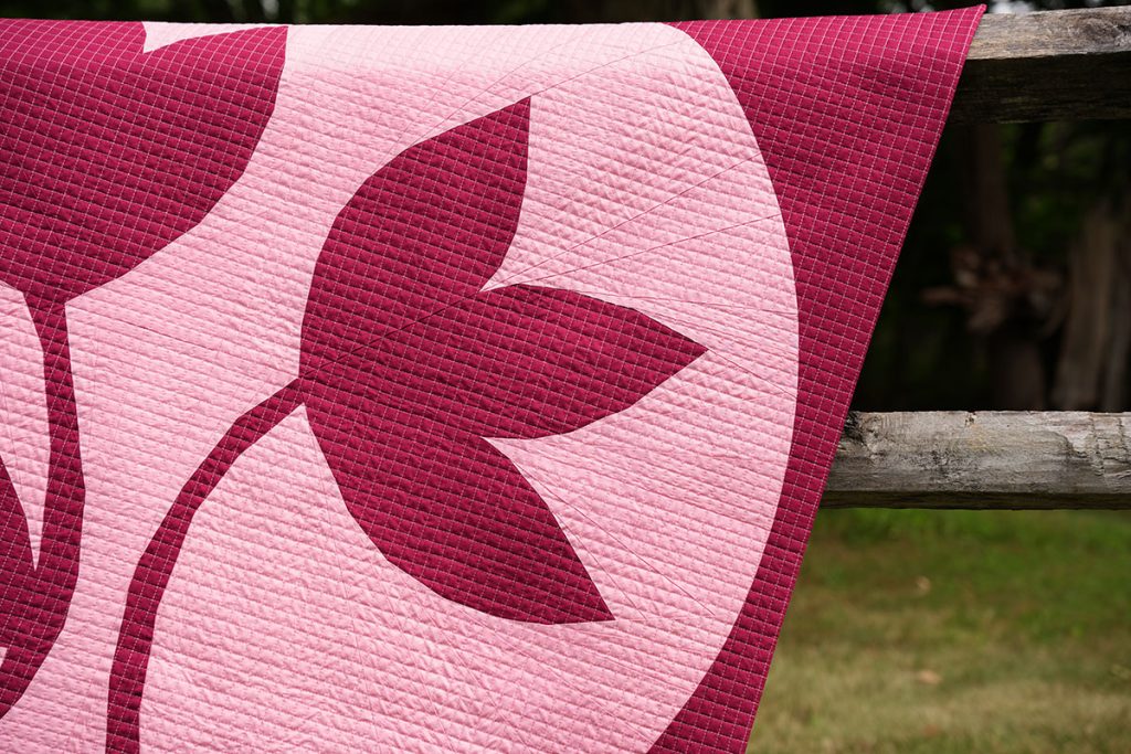 Close-up of a portion of Flower Moon quilt in dark red and peachy pink draped over a fence.